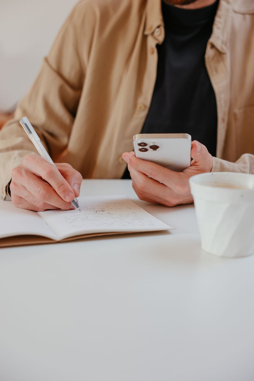 homme qui écrit sur un cahier, avec un téléphone à la main